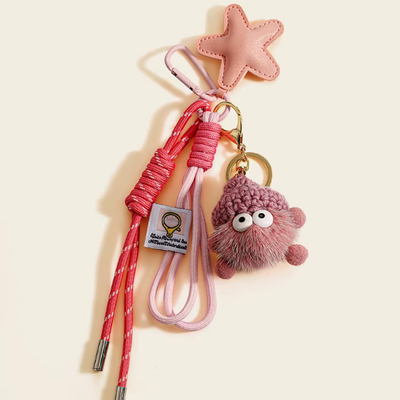 Pink keychain with a plush toy and star-shaped object on a beige background