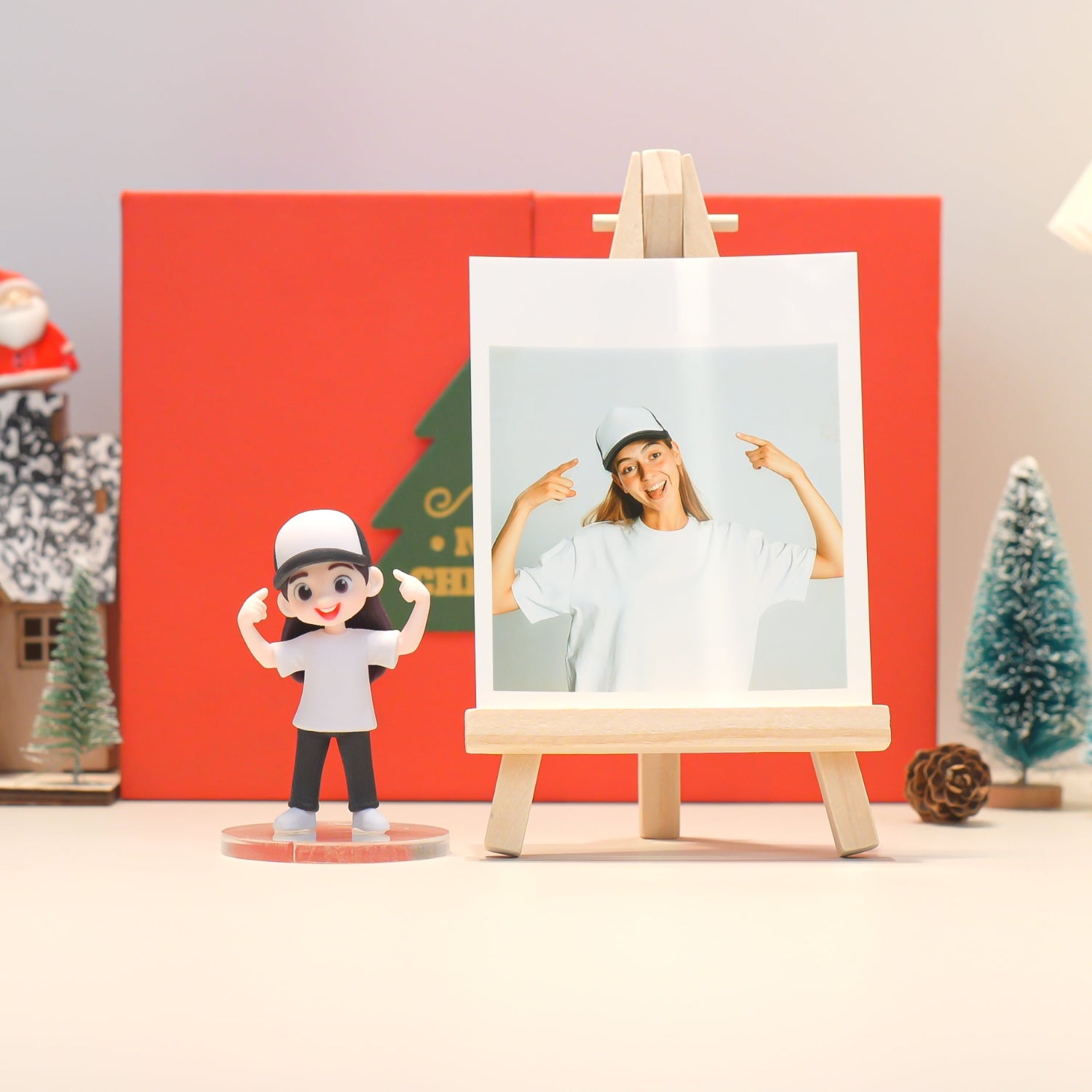 Figurine of a person in a white shirt and black pants standing next to a photo on an easel with a red background and Christmas decorations.