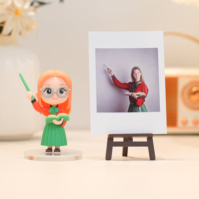 Figurine of a person with red hair and glasses holding a green wand, standing next to a photo on an easel.