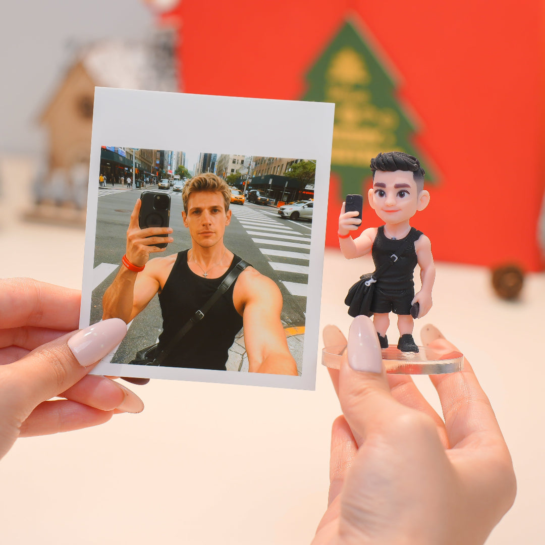 Person holding a photo of a man taking a selfie with a matching action figure in front of a blurred city street background.