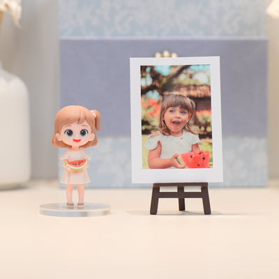 Figurine of a girl holding a watermelon next to a photo of a child on an easel.