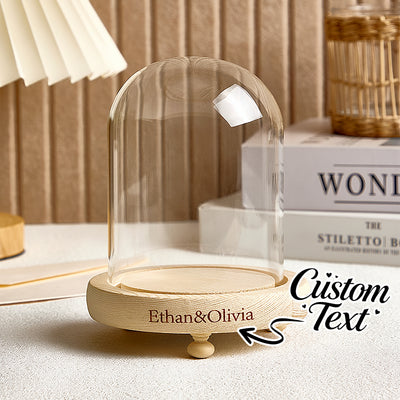 Decorative glass dome with wooden base on a surface, featuring personalized text.