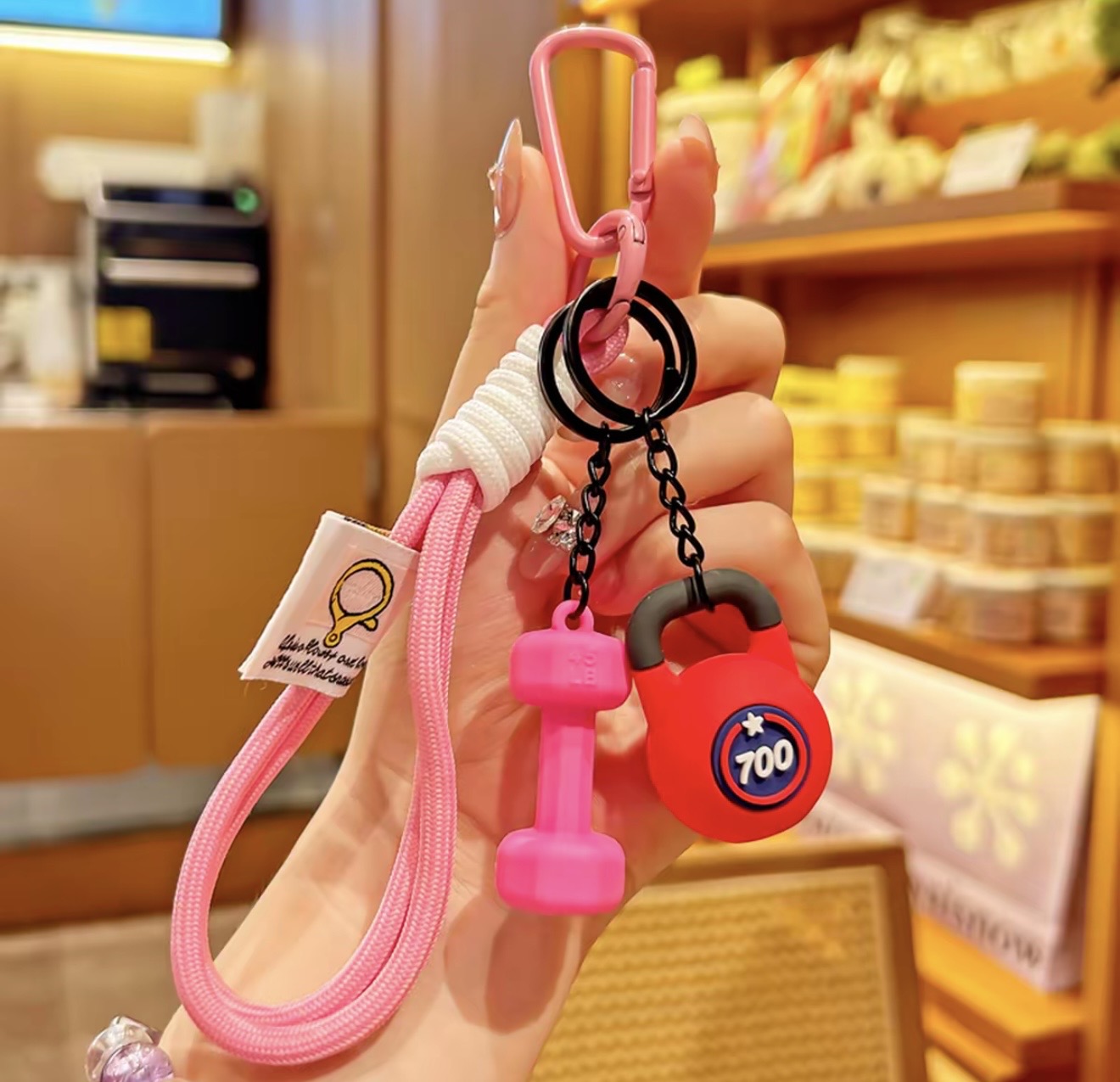 Hand holding a keychain with pink and red charms in a store setting