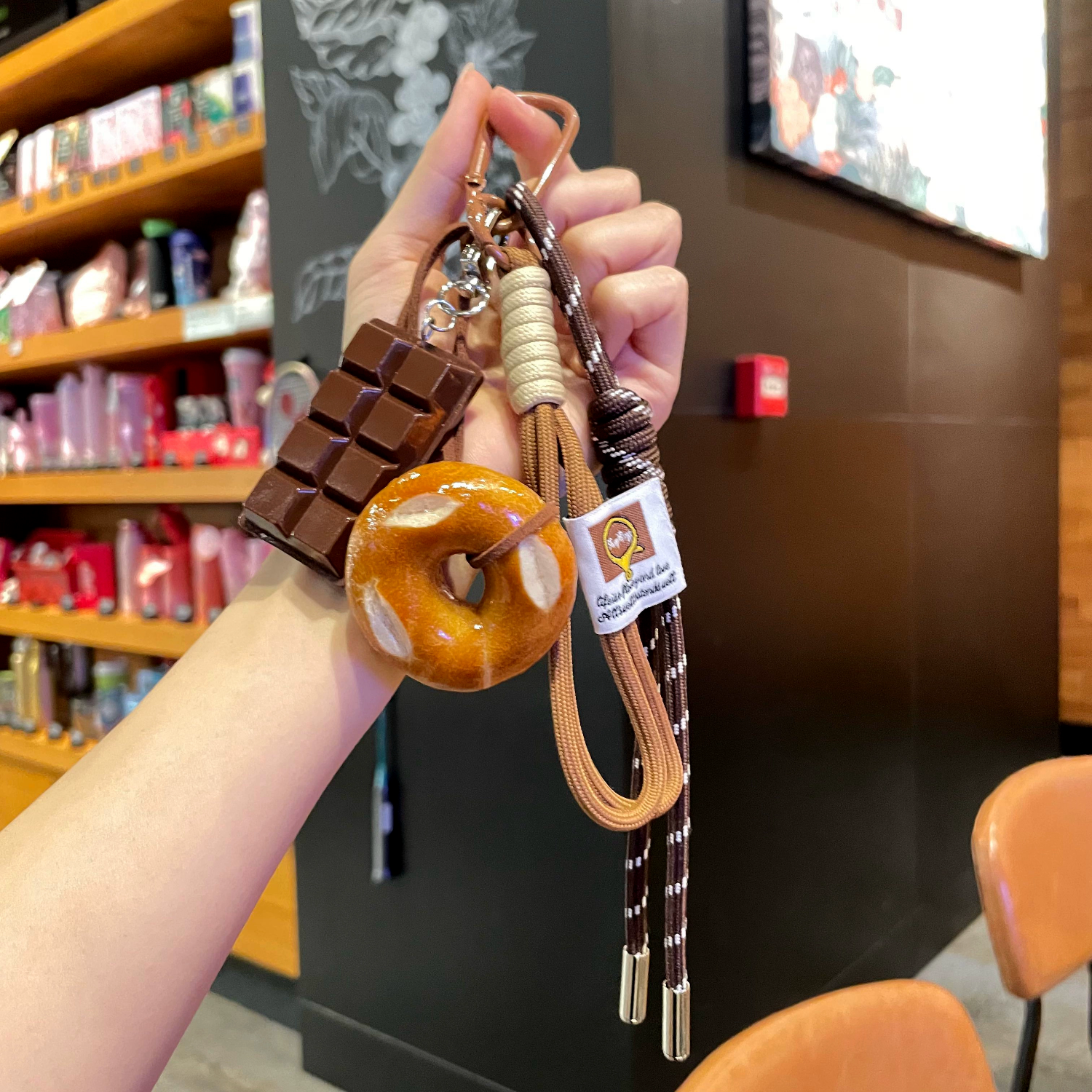 Hand holding a keychain with chocolate bar and donut design in a store setting