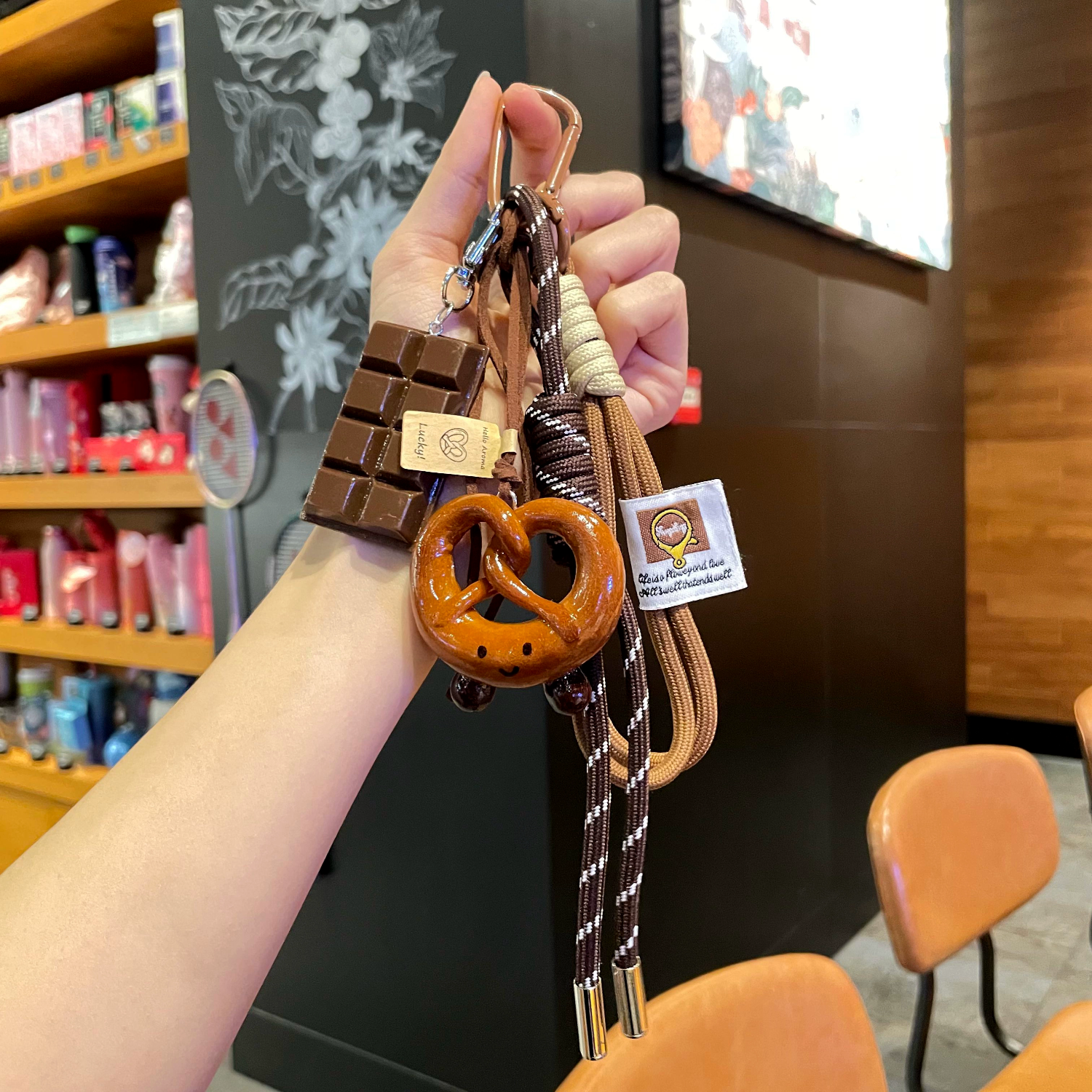 Hand holding a keychain with a chocolate bar and pretzel design in a store setting.