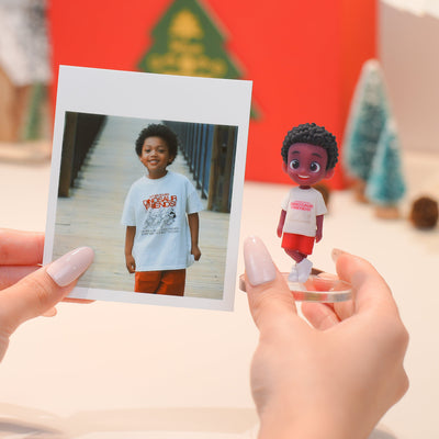 Person holding a photo of a child and a corresponding action figure with a Christmas tree in the background