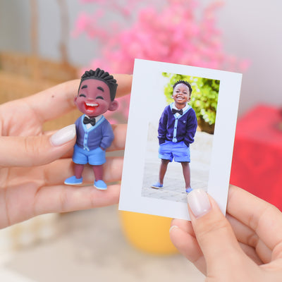Hand holding a figurine of a child in a blue outfit next to a photo of the same child outdoors.