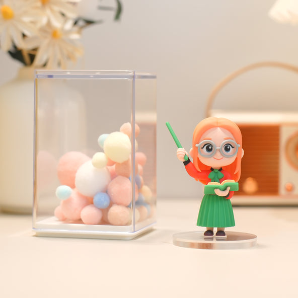 Figurine of a character with red hair and glasses holding a green wand, next to a transparent box with colorful balls.