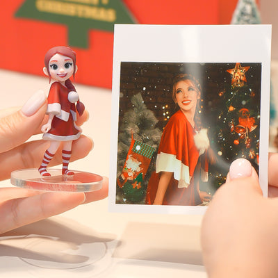 Person holding a Christmas-themed figurine and photo of a woman in a red coat by a Christmas tree.