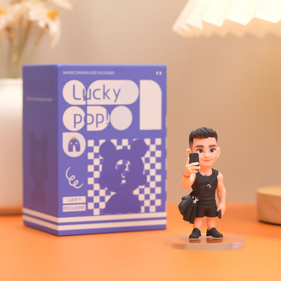Figurine of a person holding a phone next to a 'Lucky Pop!' box on a table.