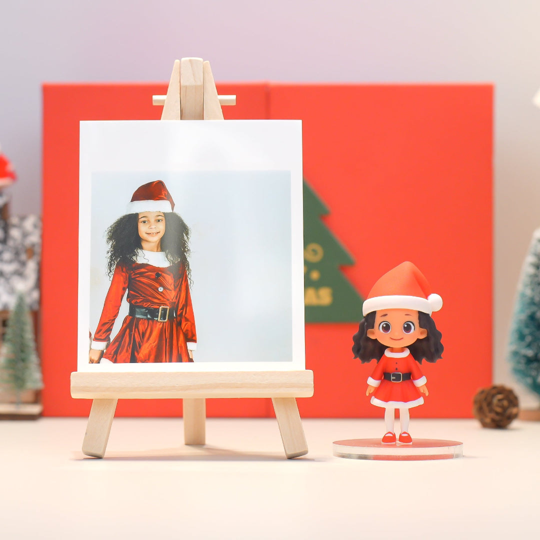 Christmas-themed figurine of a girl in a red dress and Santa hat next to a photo of a girl in a similar outfit on an easel.