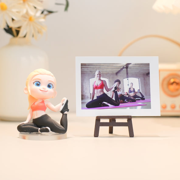 Figurine of a woman in a yoga pose next to a digital photo frame displaying a yoga class video.