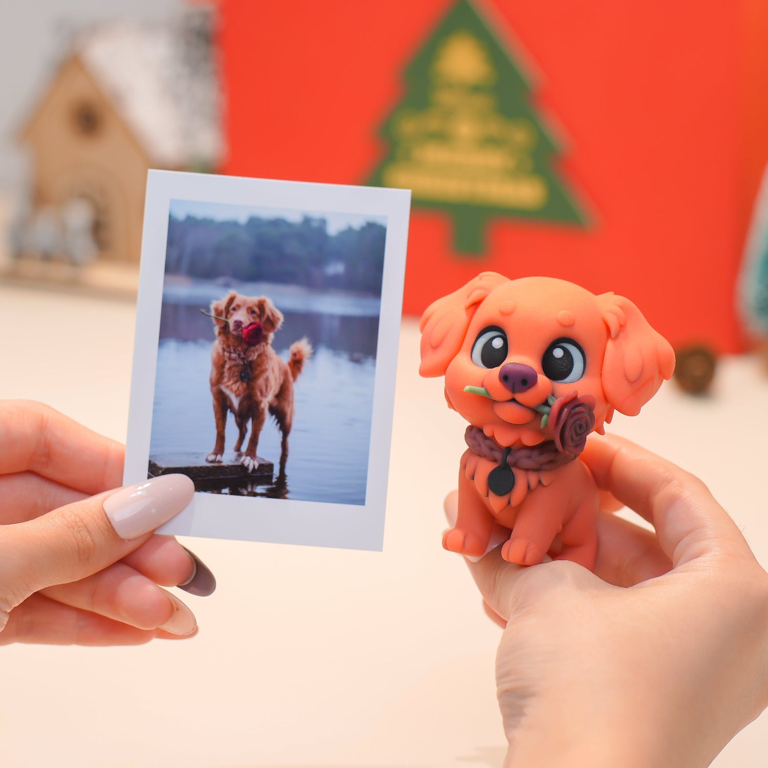 Hand holding a photograph of a dog by a lake next to a small orange dog figurine.