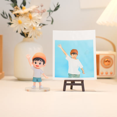 Figurine of a boy with a matching photo on a stand, with a vase and lamp in the background.