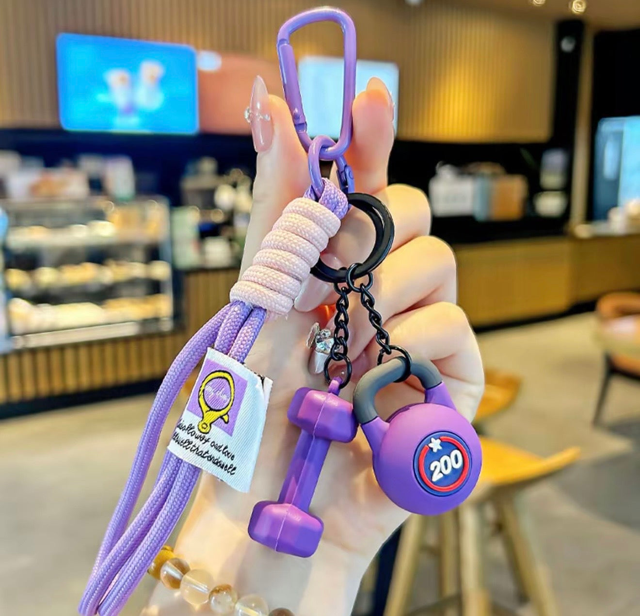 Purple keychain with fitness-themed design held by a hand in a blurred indoor setting