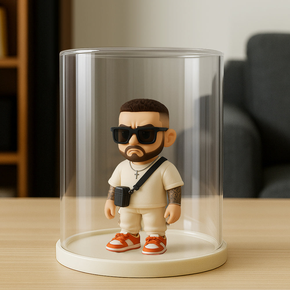 Toy figure of a person with sunglasses and a camera inside a clear cylindrical display case on a wooden surface.