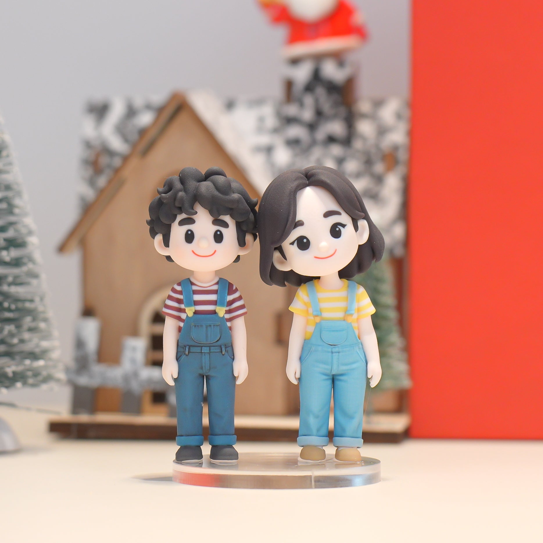 Two figurines of a boy and girl in overalls standing on a stand with a festive background.