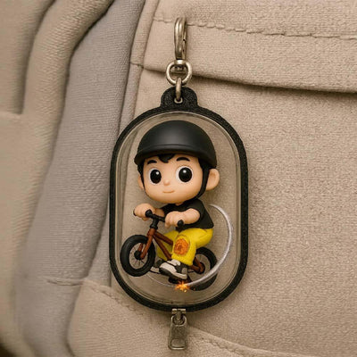 Keychain with a cartoon character riding a bike attached to a beige bag.