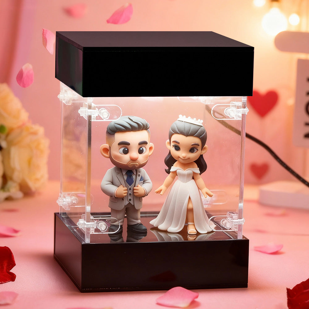 Wedding-themed figurines in a clear display case on a pink background with heart decorations.