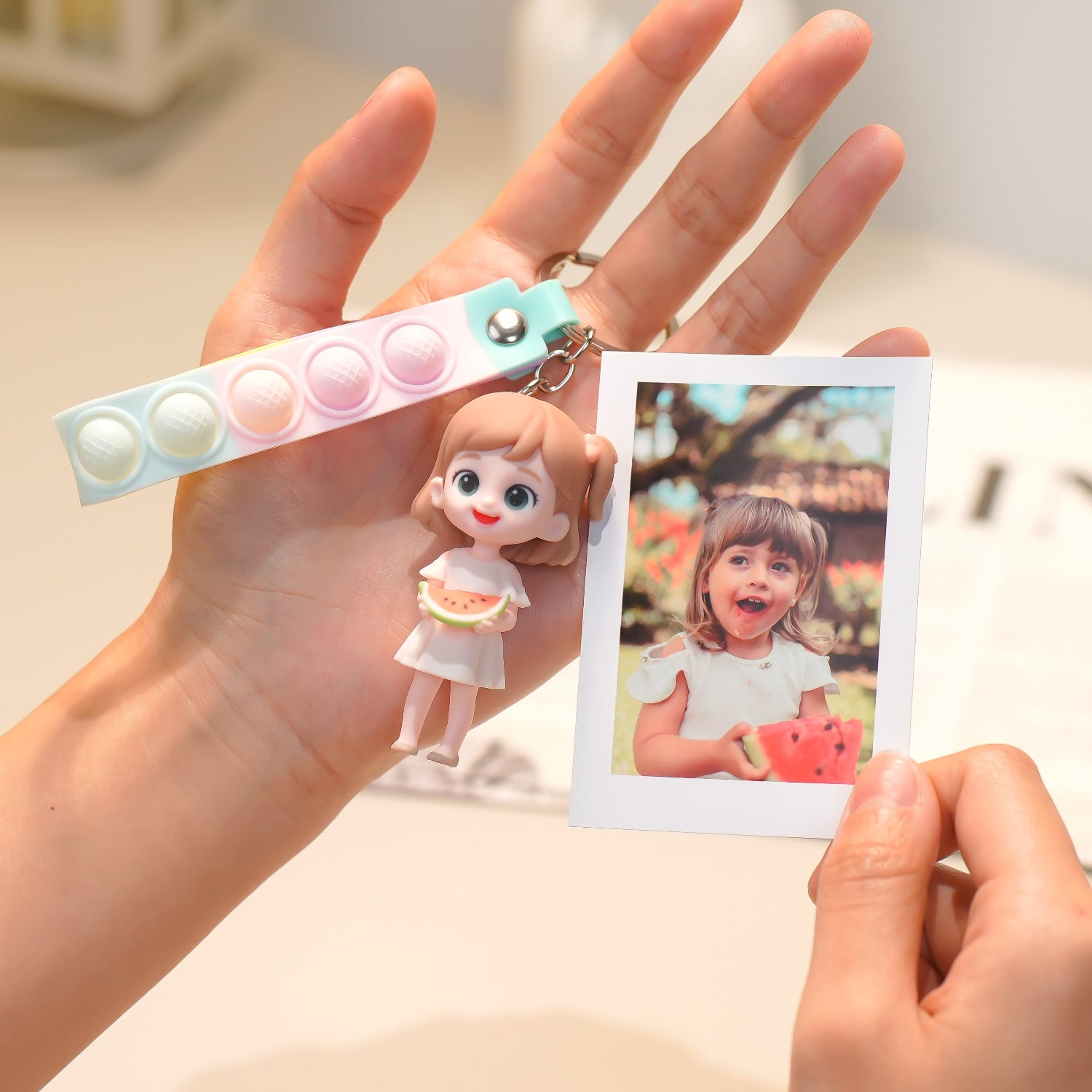 Hand holding a keychain with a small doll figure and a photo of a child eating watermelon.