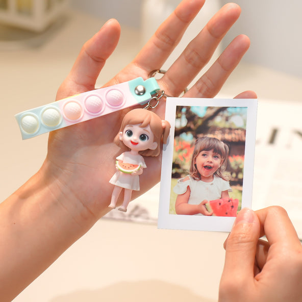 Hand holding a keychain with a small doll figure and a photo of a child eating watermelon.