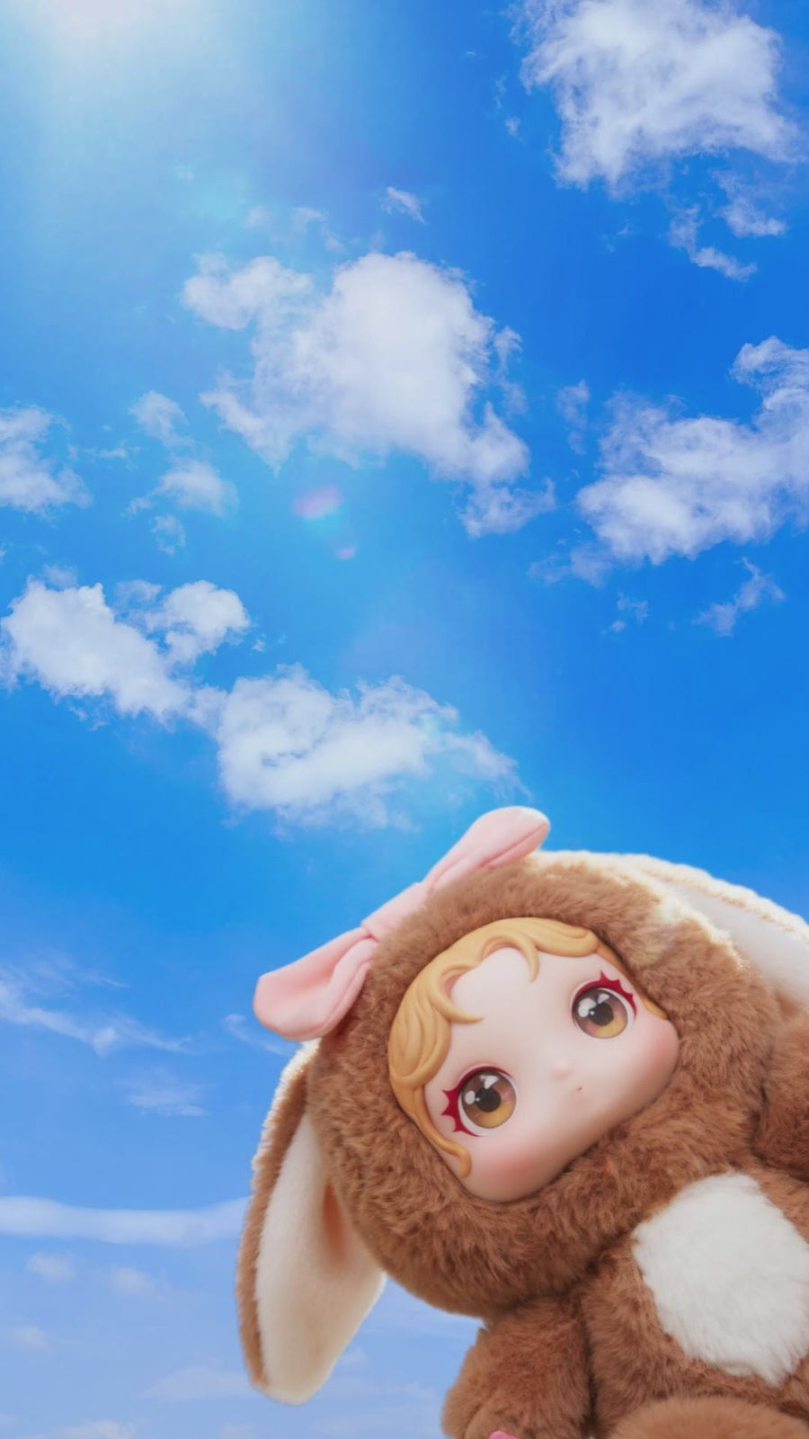 Hand holding a custom plush doll with bunny ears outdoors in a grassy field